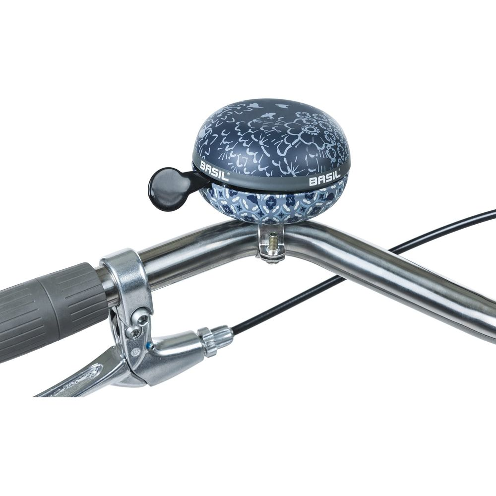 Eine blaue Fahrradklingel mit Blumenmuster ist am silbernen Lenker montiert.