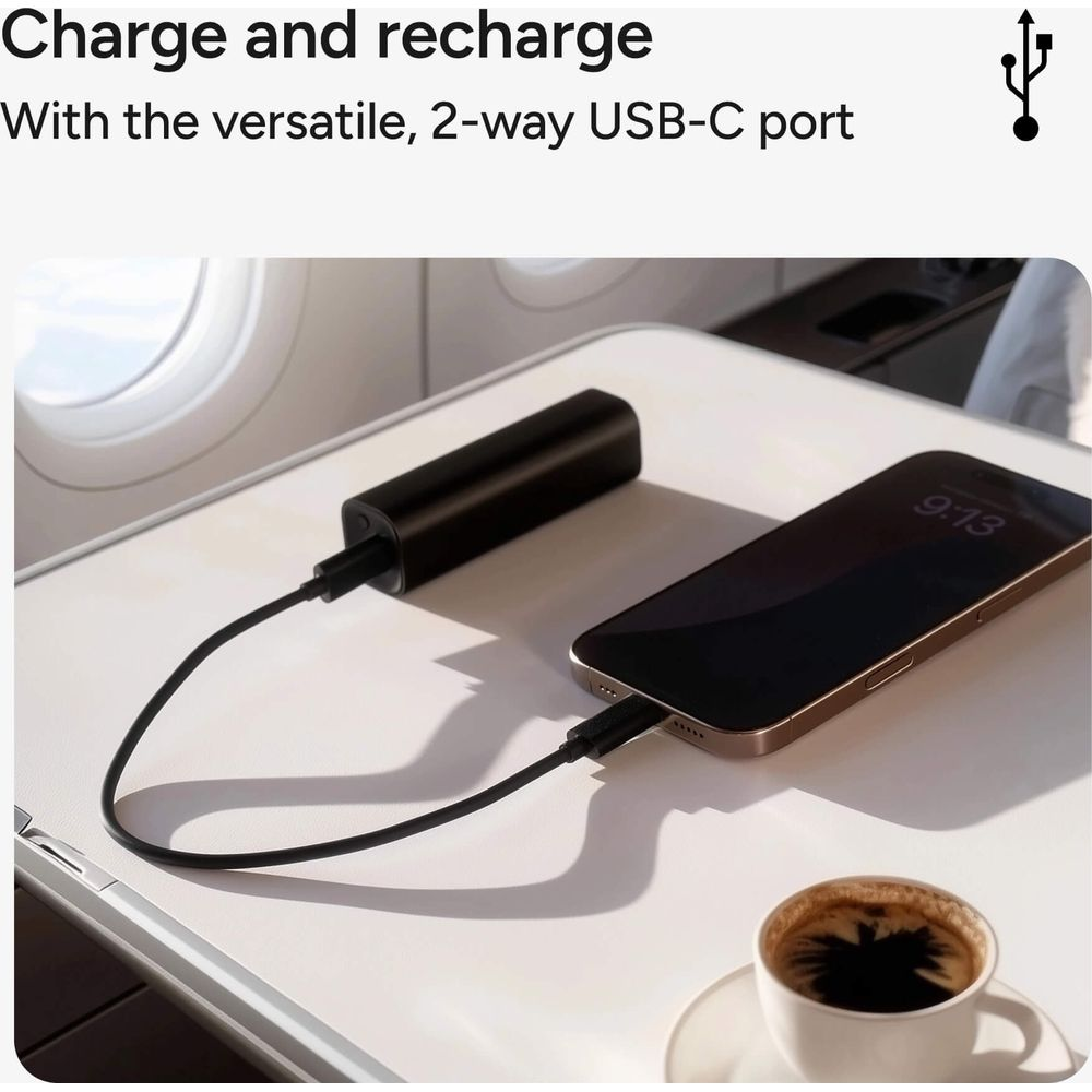 Ein schwarzer Akku lädt ein Smartphone auf einem Flugzeugtisch. Kaffee daneben.