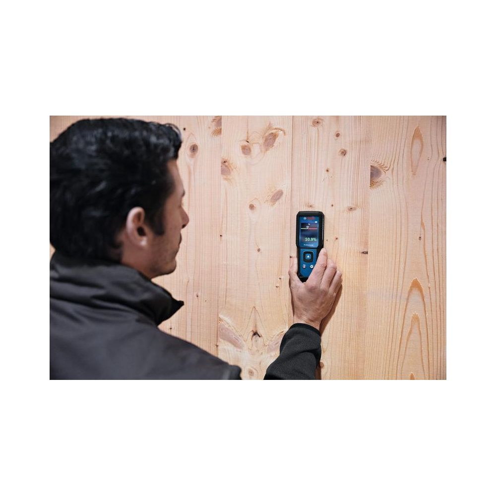 Mann misst Holzfeuchte mit Gerät an Holzwand.