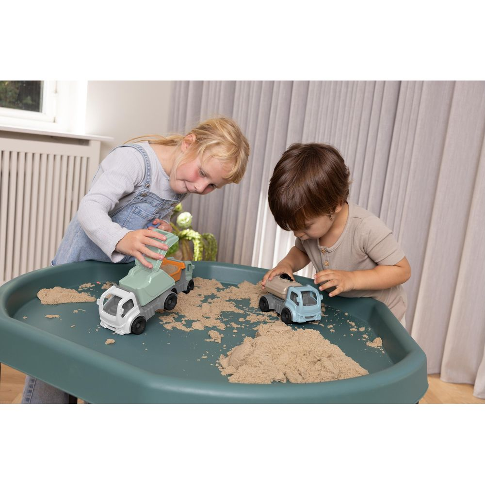 Zwei Kinder spielen mit Sand und Spielzeug LKWs in einer Sandwanne.
