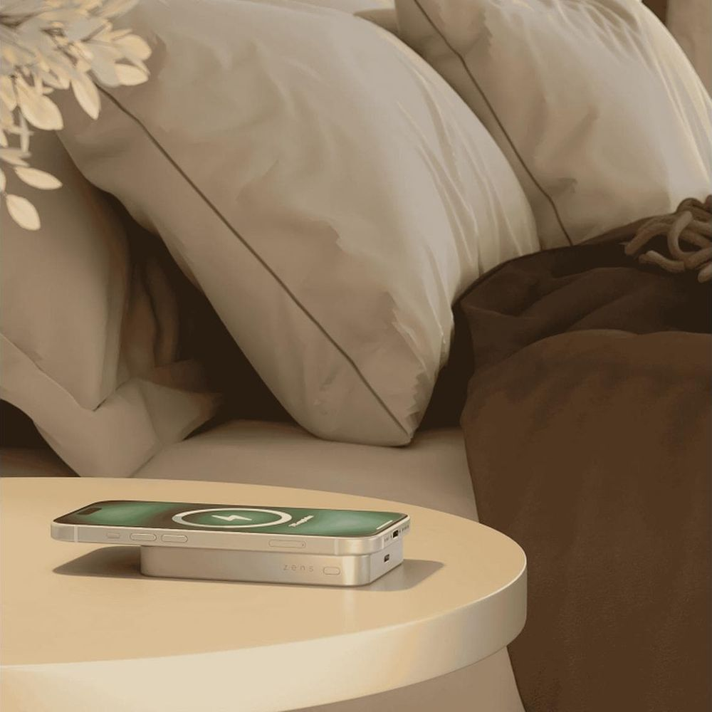 Ein weißes kabelloses Ladegerät mit einem Telefon darauf steht auf einem runden Tisch neben einem Bett.