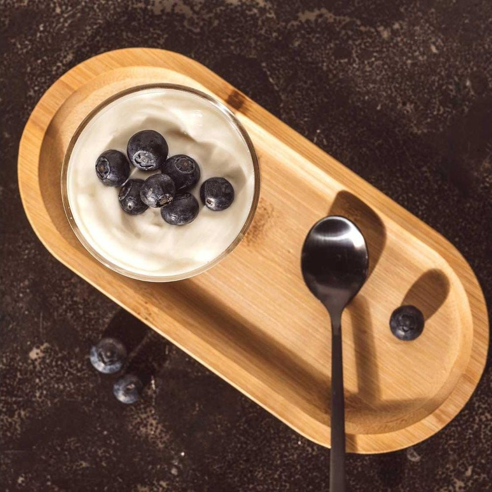 Ein Glas Joghurt mit Blaubeeren auf einem Holzteller mit Löffel.