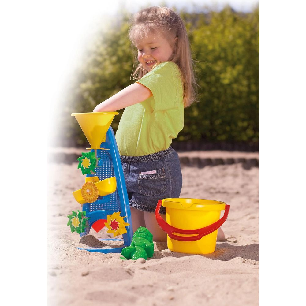 Ein kleines Mädchen spielt mit einem Spielzeug-Wasserspielzeug im Sand, mit einem gelben Eimer.