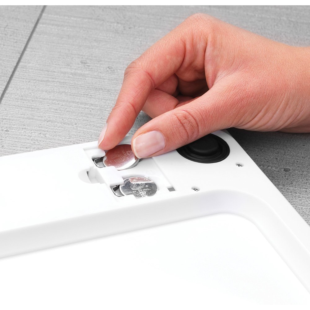 Eine Hand setzt eine Knopfzellenbatterie in ein weißes Gerät ein.