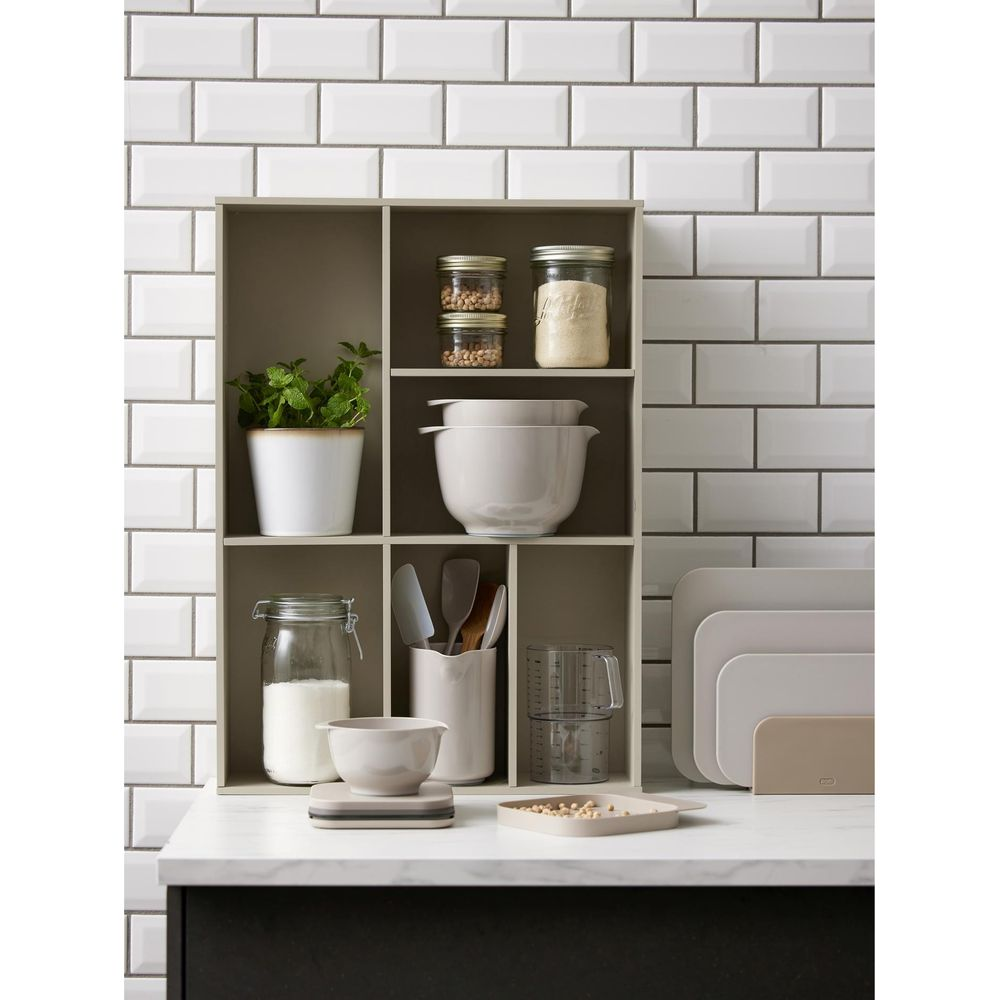 Küchenregal mit Gläsern, Schüsseln, Pflanze, Utensilien und Backblechen.