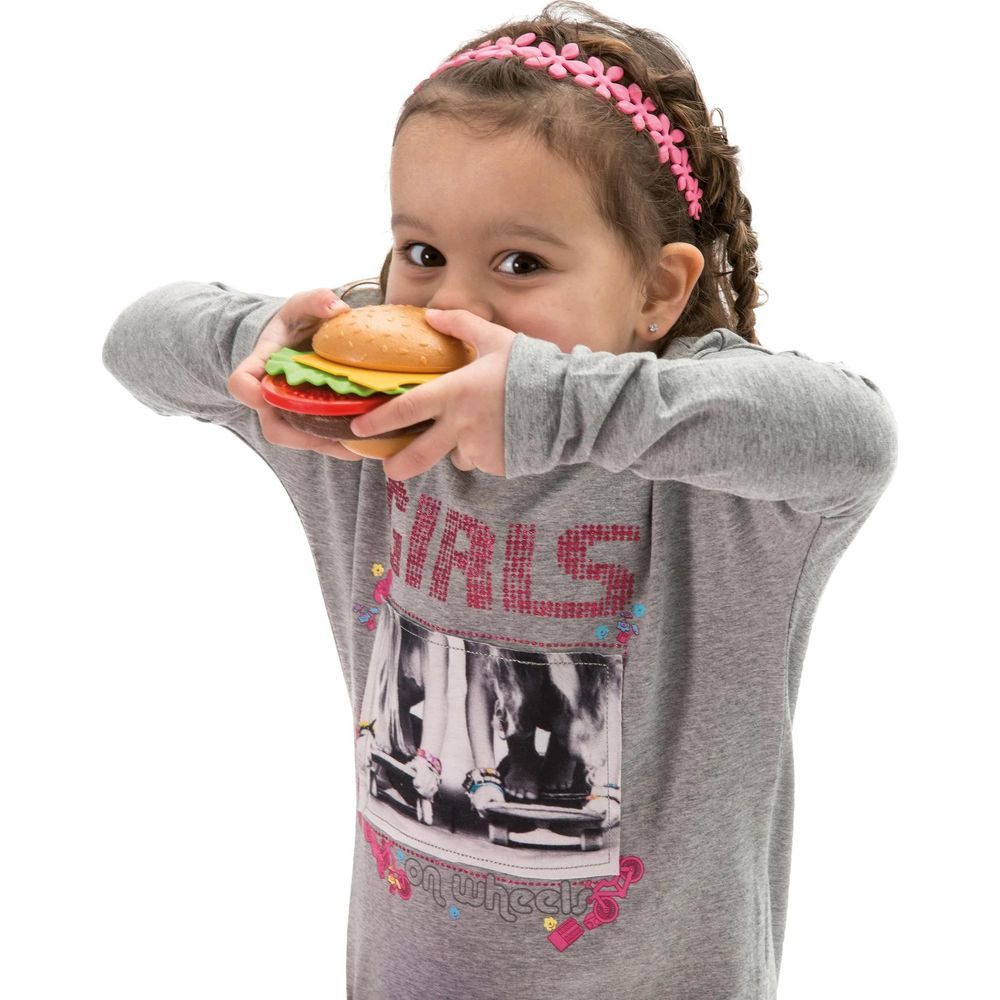 Ein junges Mädchen mit einem rosa Stirnband hält einen Spielzeugburger an ihren Mund.