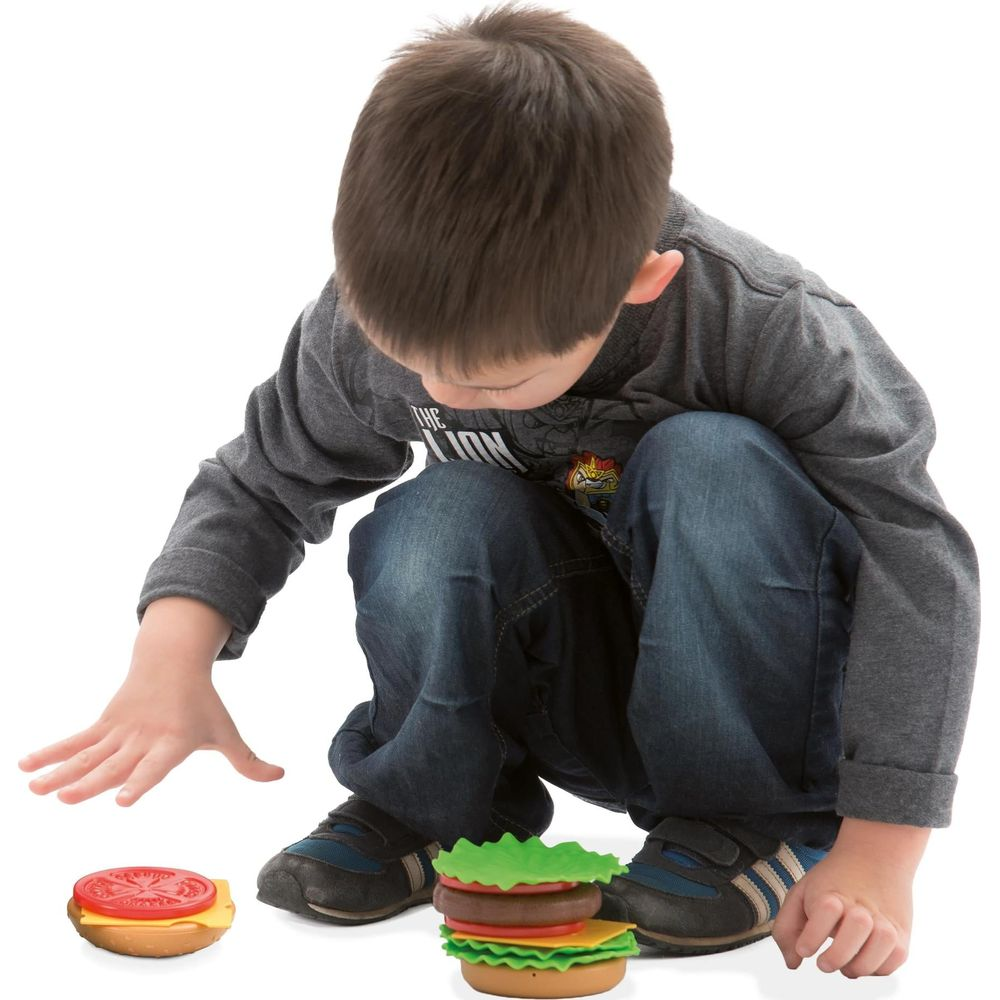 Ein Junge spielt mit Spielzeug-Burgern auf weißem Hintergrund.