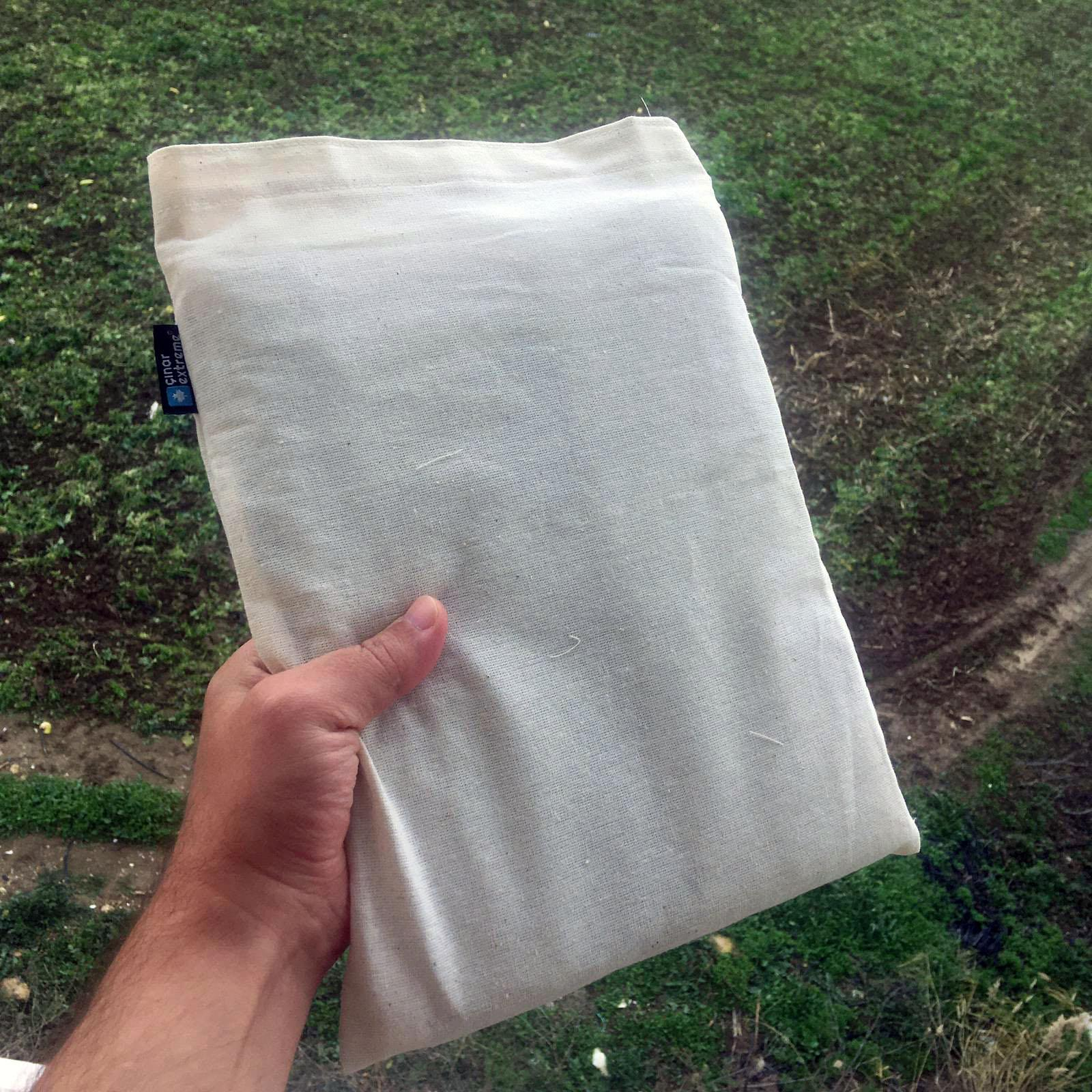 Bir el, yeşil çimlerin önünde beyaz bir kumaş çanta tutuyor.
