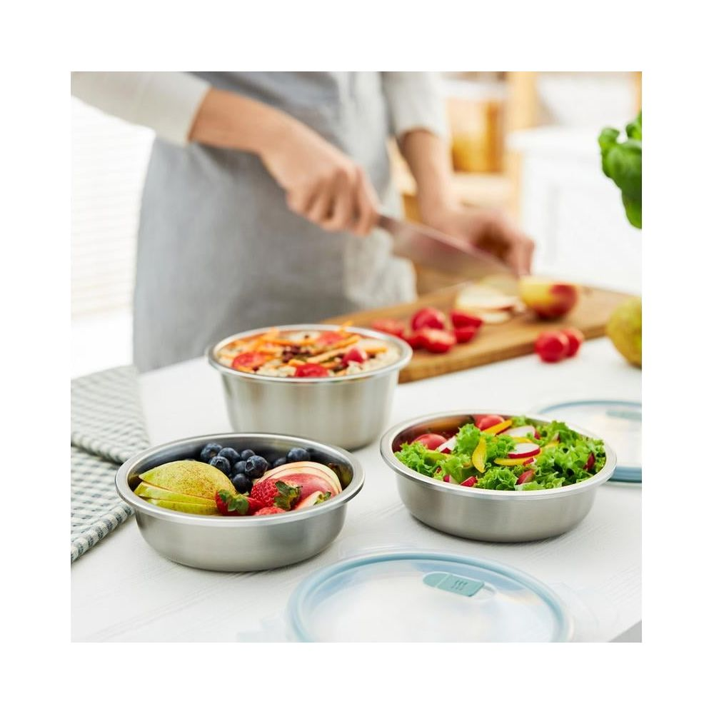 Ciotole in acciaio inox con frutta, insalata e un pasto; una persona taglia mele.
