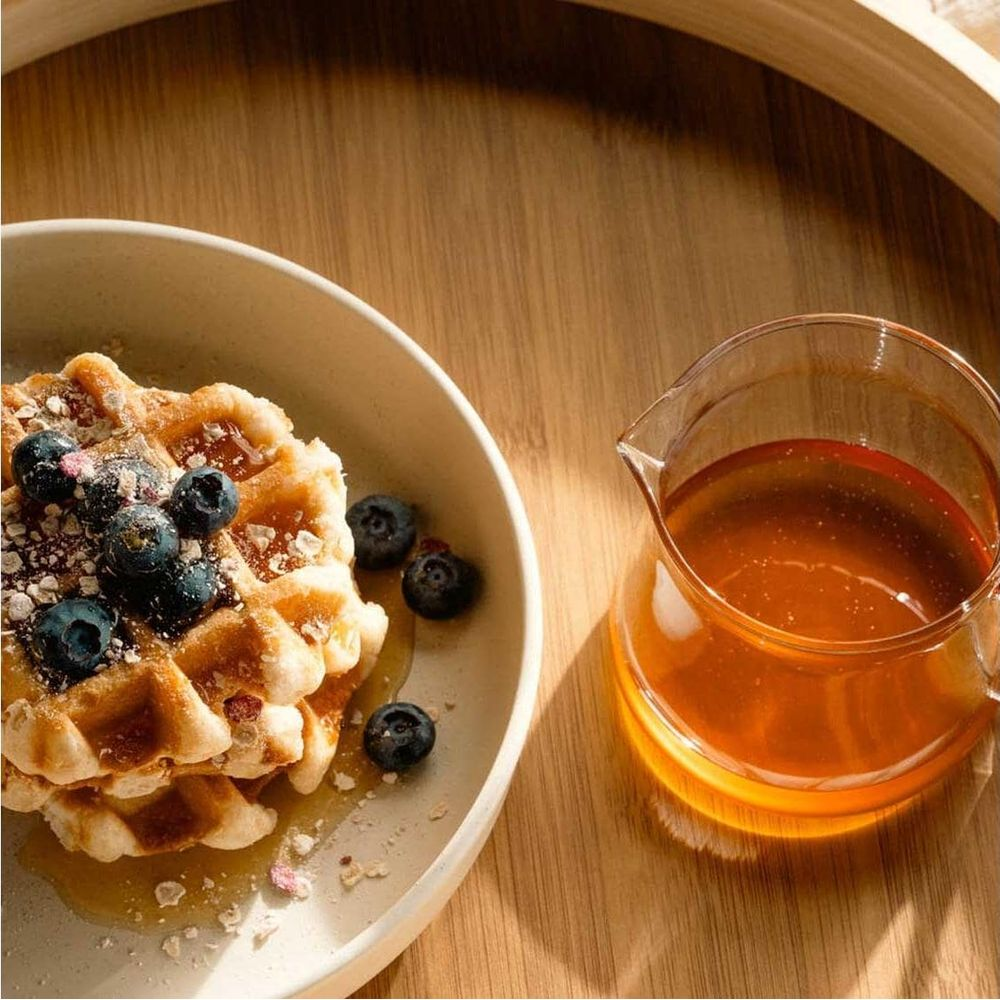 Zwei Waffeln mit Blaubeeren und Honig in einem Krug auf einem Holztisch.