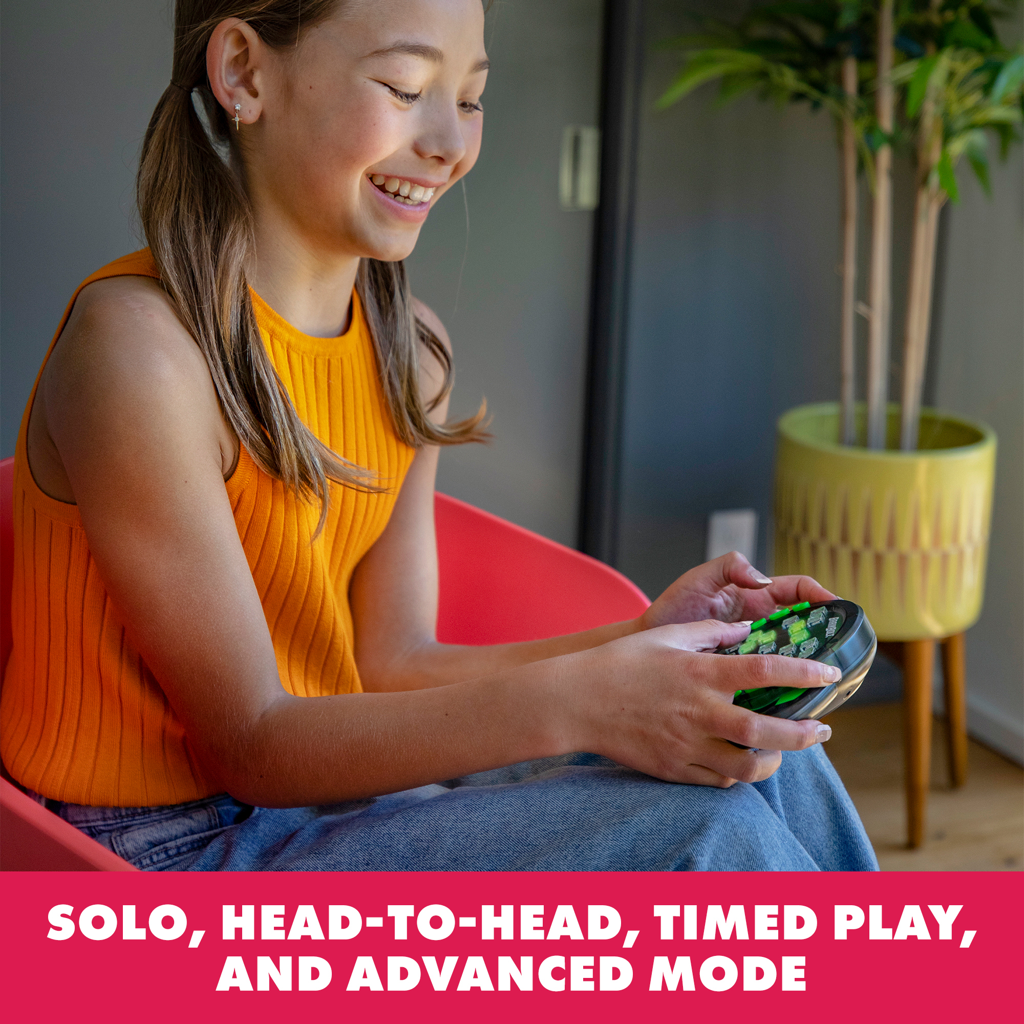 Ein junges Mädchen in einem orangen Oberteil spielt mit einem schwarzen Handheld-Spielgerät.