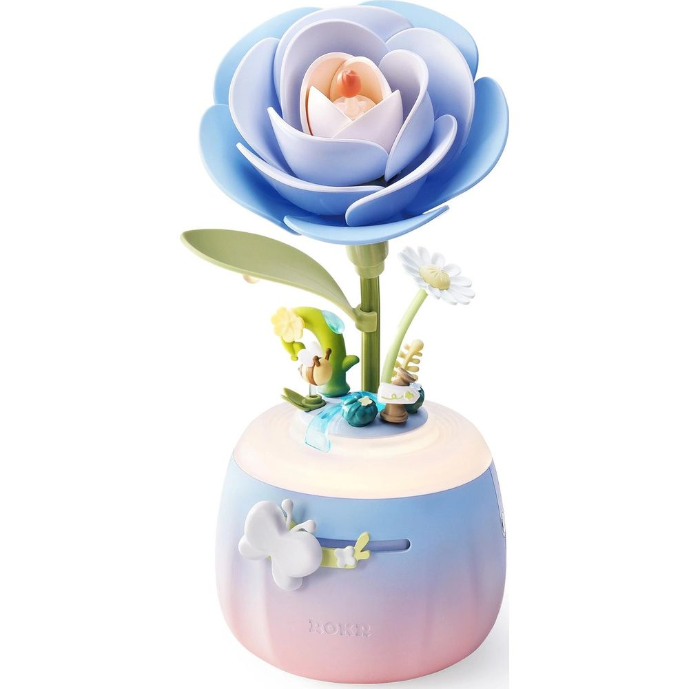 Eine blaue Rose mit Miniaturfiguren und Schmetterling auf einer beleuchteten Basis.