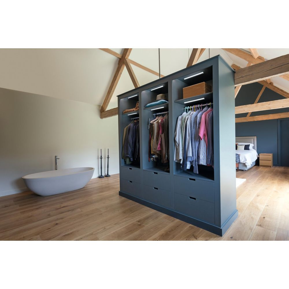 Ein begehbarer Kleiderschrank mit Kleidung und Schubladen neben einer Badewanne und einem Bett.