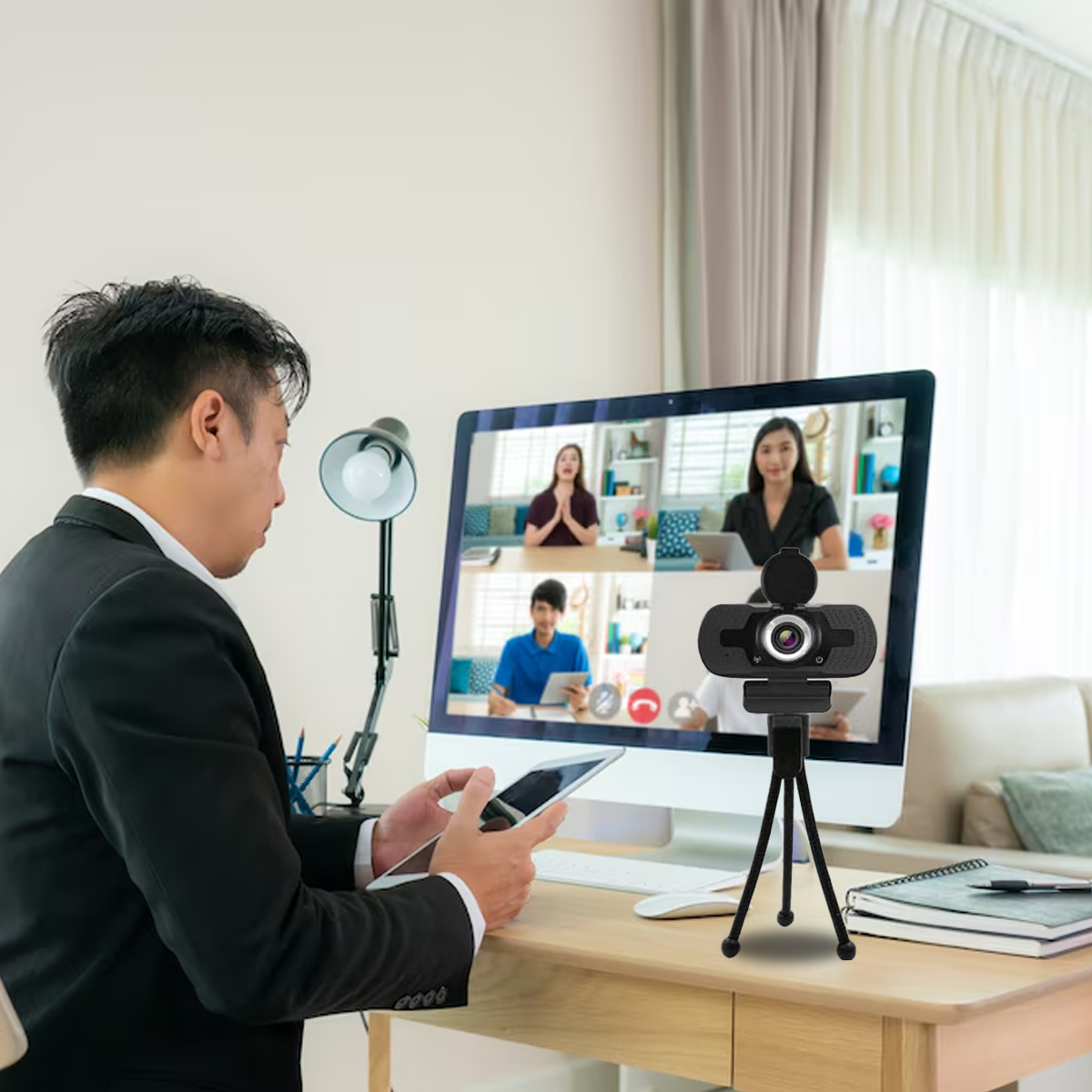 Mann bei Videokonferenz. Mann hält Tablet. Webcam auf Stativ.