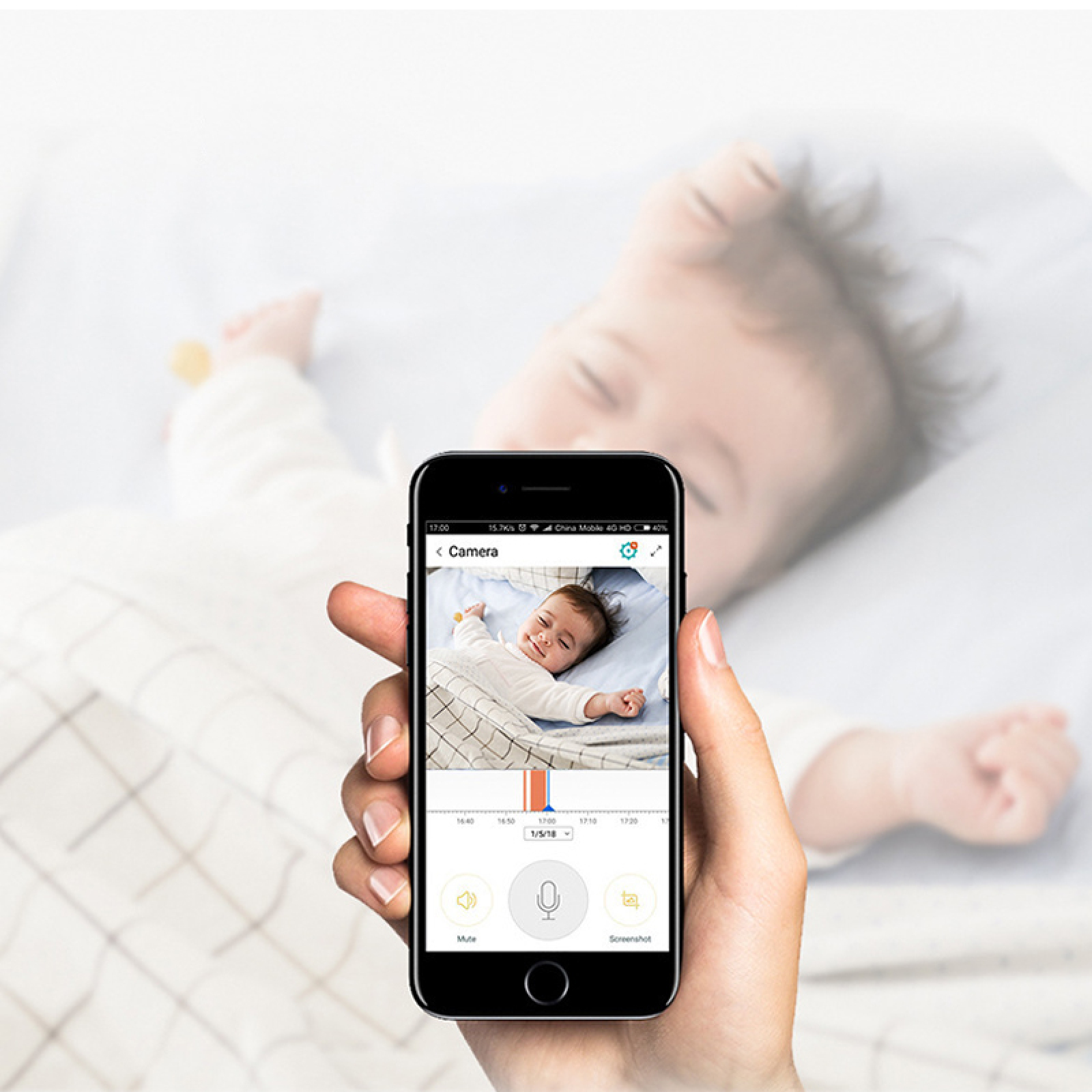 Hand hält ein Smartphone, das ein Baby im Bett zeigt. Hintergrund unscharf.