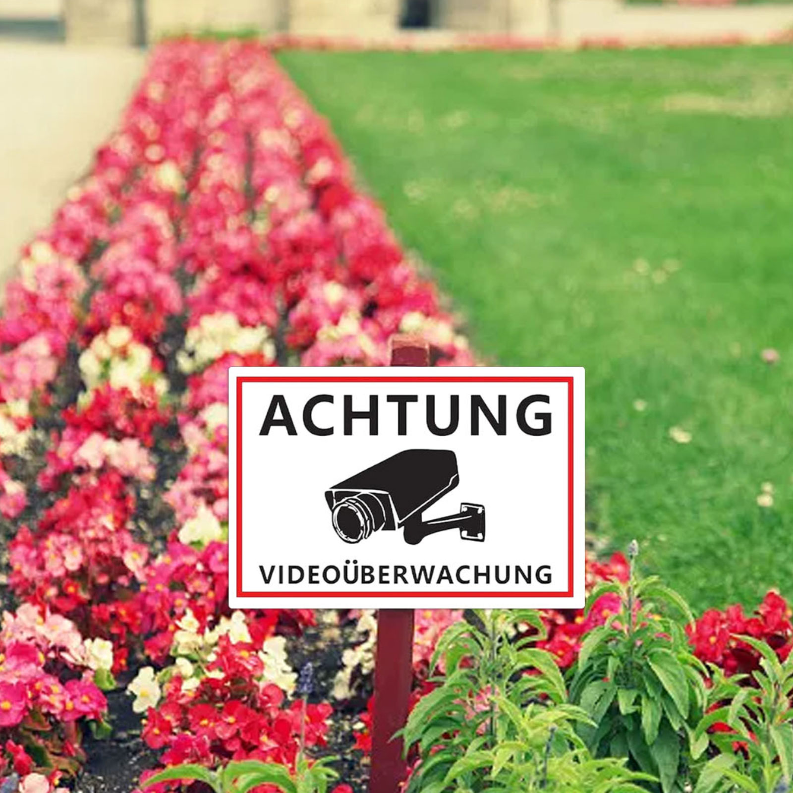 Achtung Videoüberwachung Schild neben Blumenbeet und Rasen.