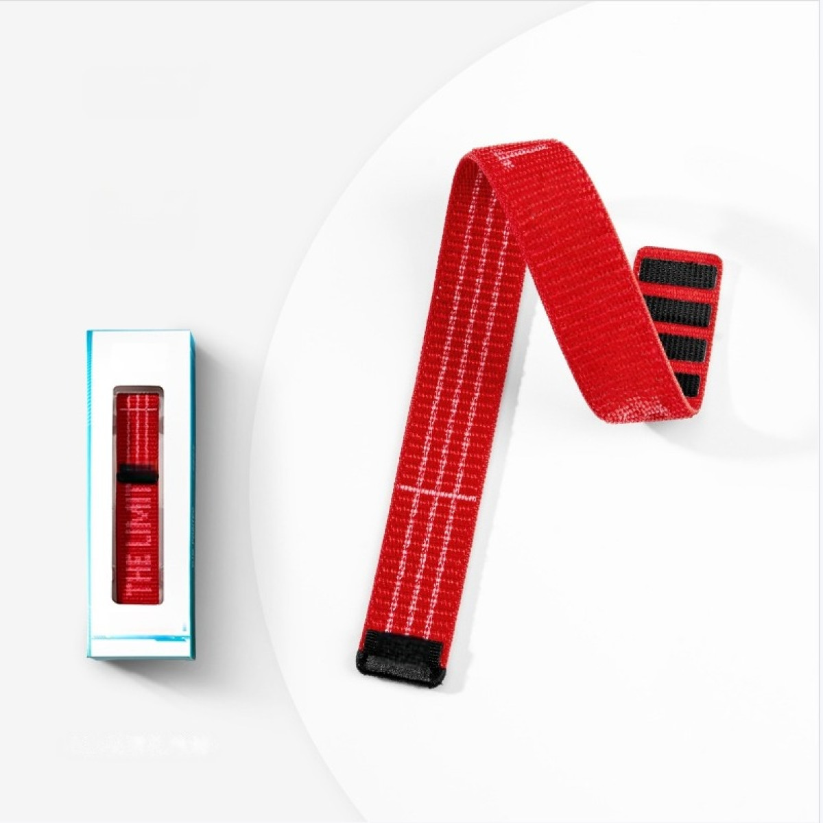 Ein rotes Gurtband mit schwarzen Streifen liegt neben einer Verpackung.