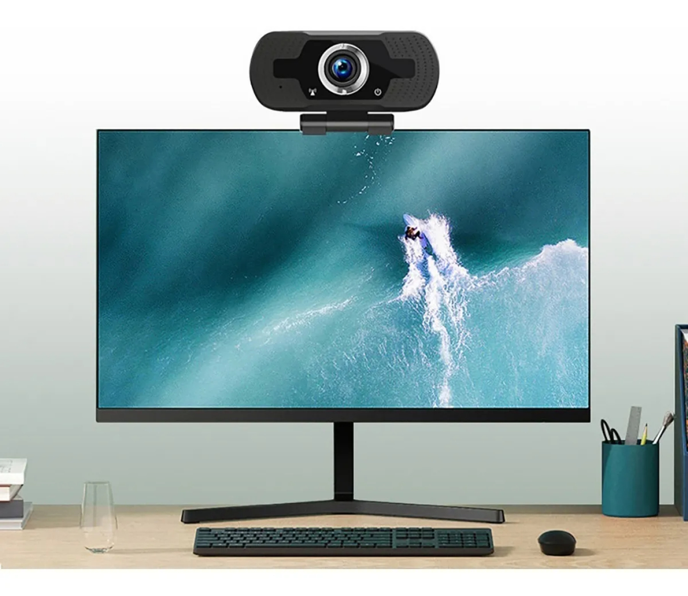 Ein Monitor mit einer Webcam zeigt einen Surfer auf einer Welle. Tastatur und Maus liegen davor.