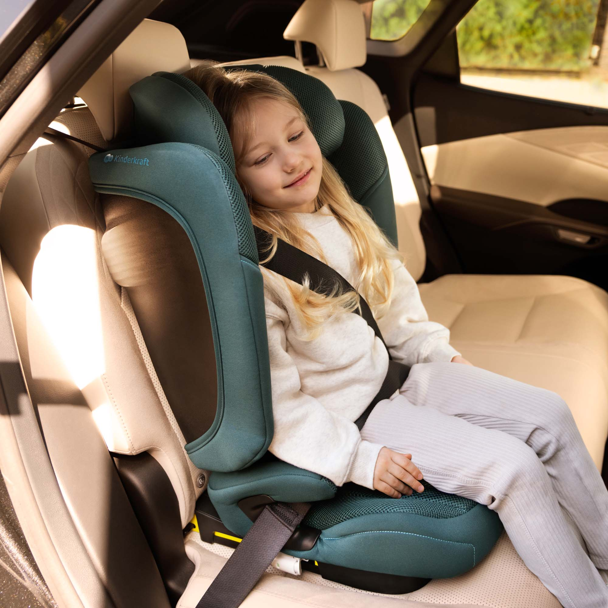 Ein kleines Mädchen schläft in einem türkisfarbenen Kindersitz im Auto.