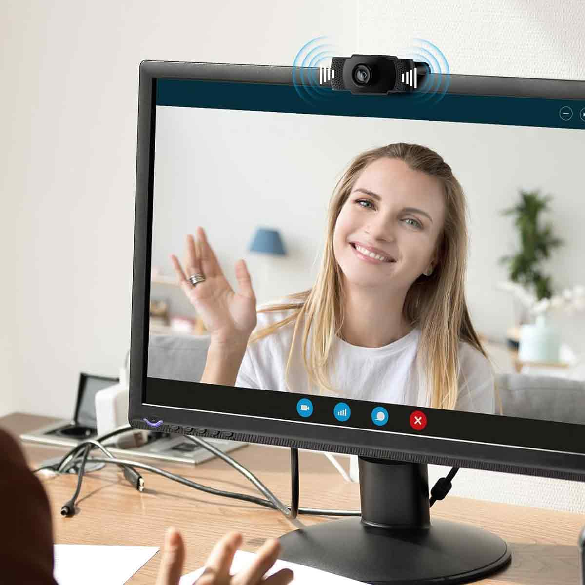 Eine Frau winkt in die Kamera, während eine Webcam über ihrem Kopf angebracht ist.