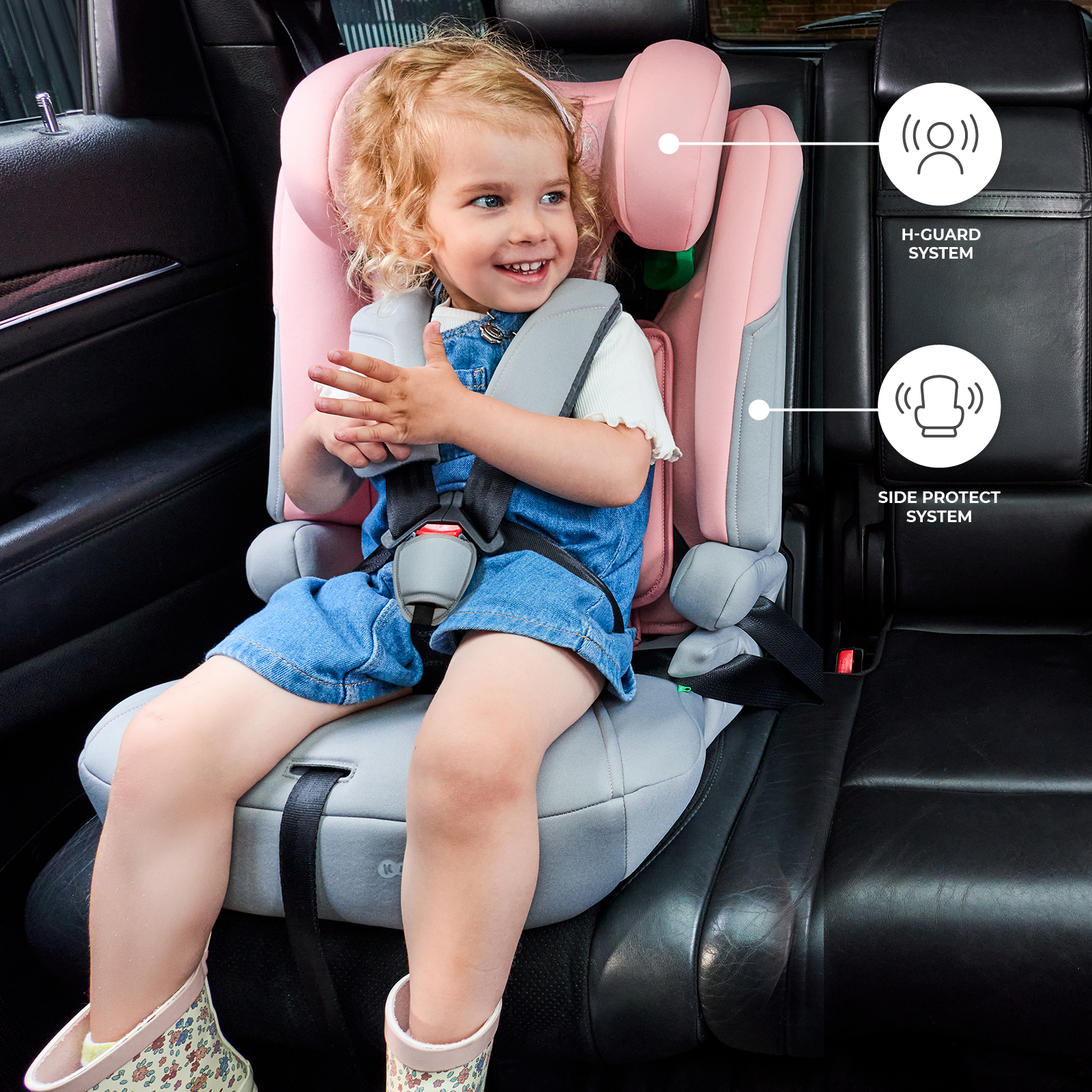 Ein kleines Mädchen sitzt in einem rosa Autositz mit einem Denim-Latzanzug.