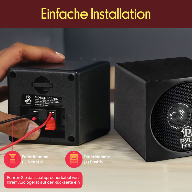 Ein schwarzer Lautsprecher mit Anschlusskabeln. Ein Finger verbindet rote und schwarze Kabel.