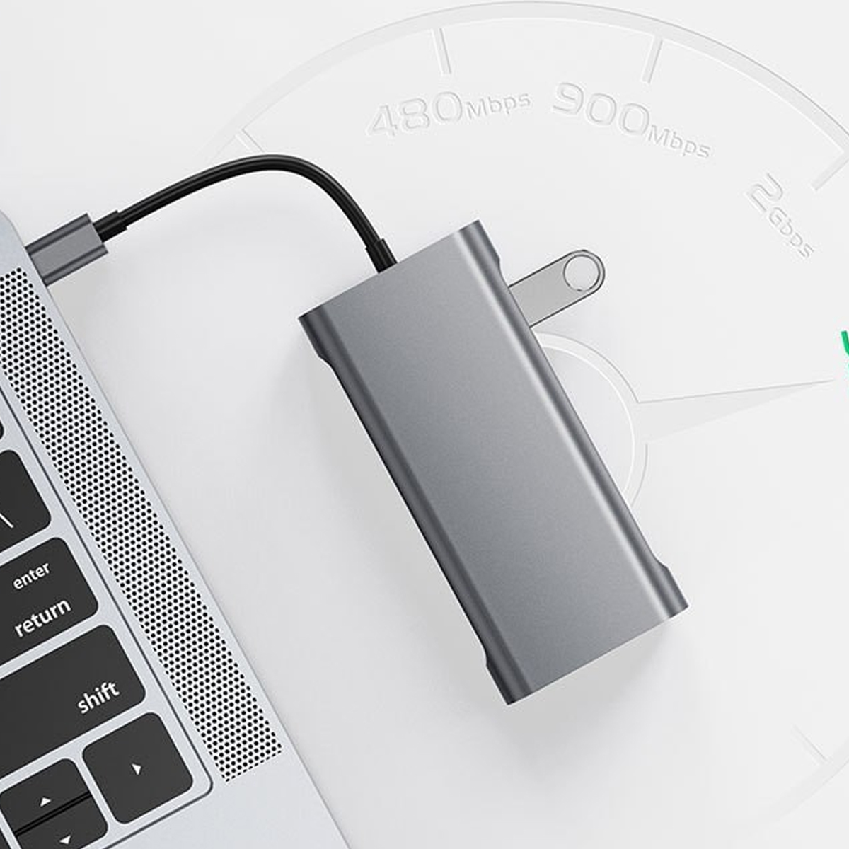 Grauer USB-C-Hub neben Laptop-Tastatur auf weißem Hintergrund mit Geschwindigkeitsanzeige.
