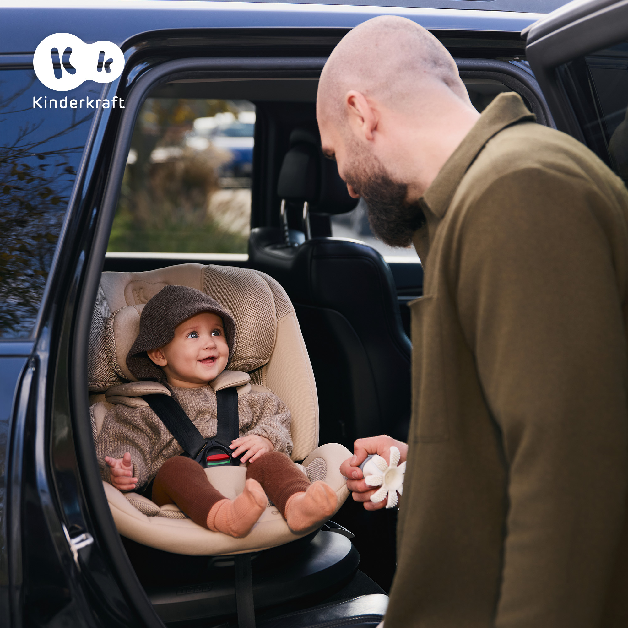Ein Mann gibt einem Baby in einem Autositz ein Spielzeug.