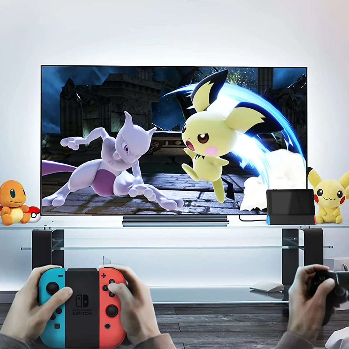 Zwei Personen spielen ein Pokémon-Spiel auf dem Fernseher, mit Plüschtieren und einer Nintendo Switch.