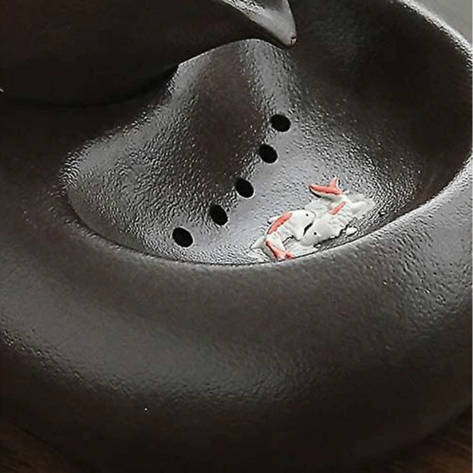 Ein dunkles, texturiertes Keramikgefäß mit kleinen, weißen und roten Fischfiguren darin.