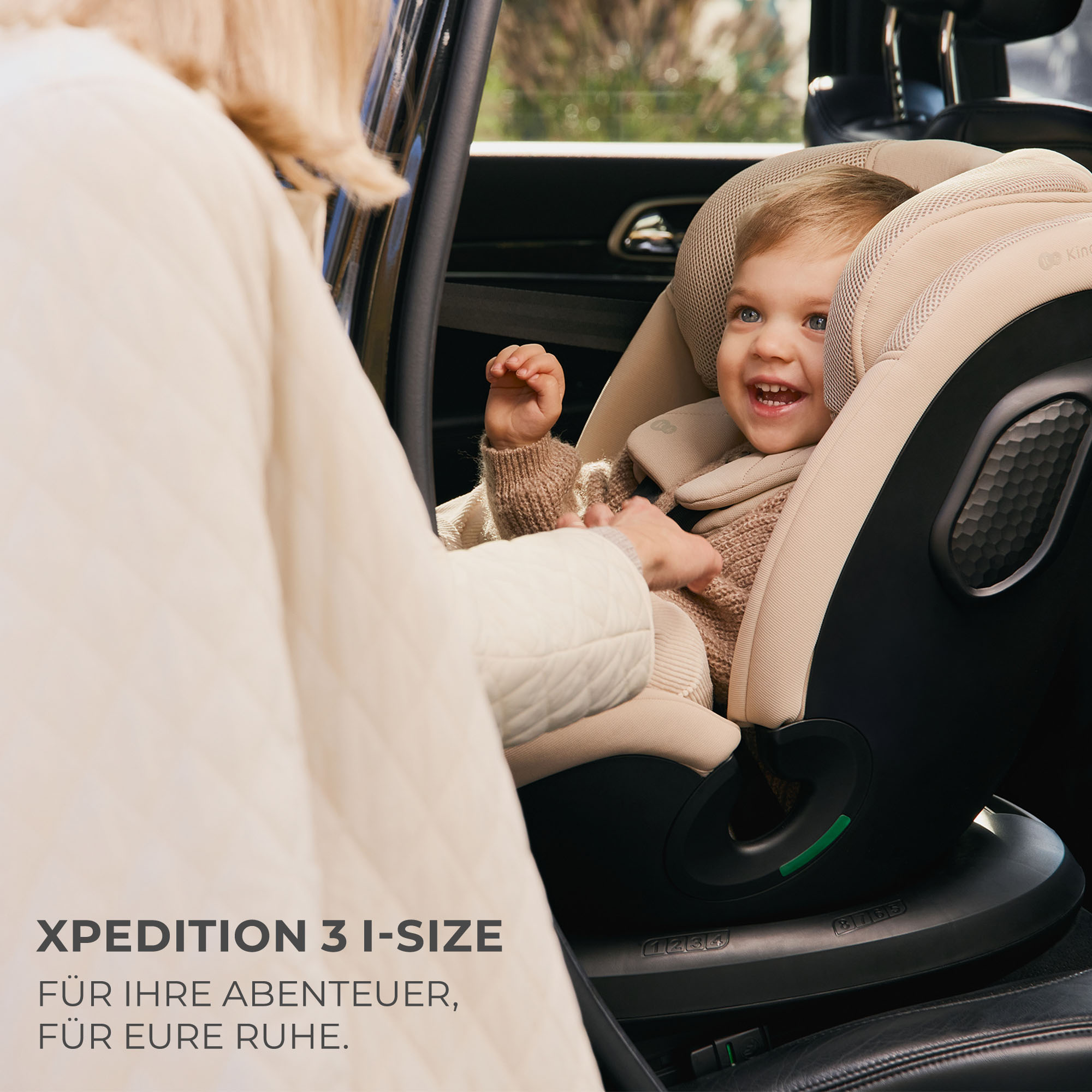 Baby im Kindersitz im Auto, Person im Vordergrund hält Gurt.