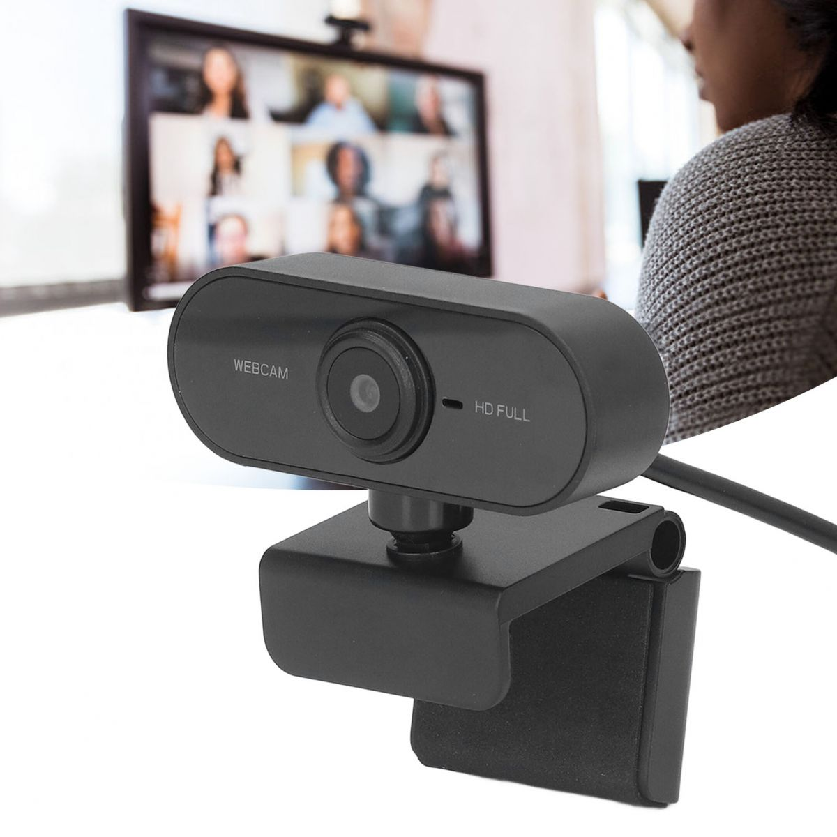 Eine schwarze Webcam steht auf einem Schreibtisch, vor einem Monitor mit Videokonferenz.