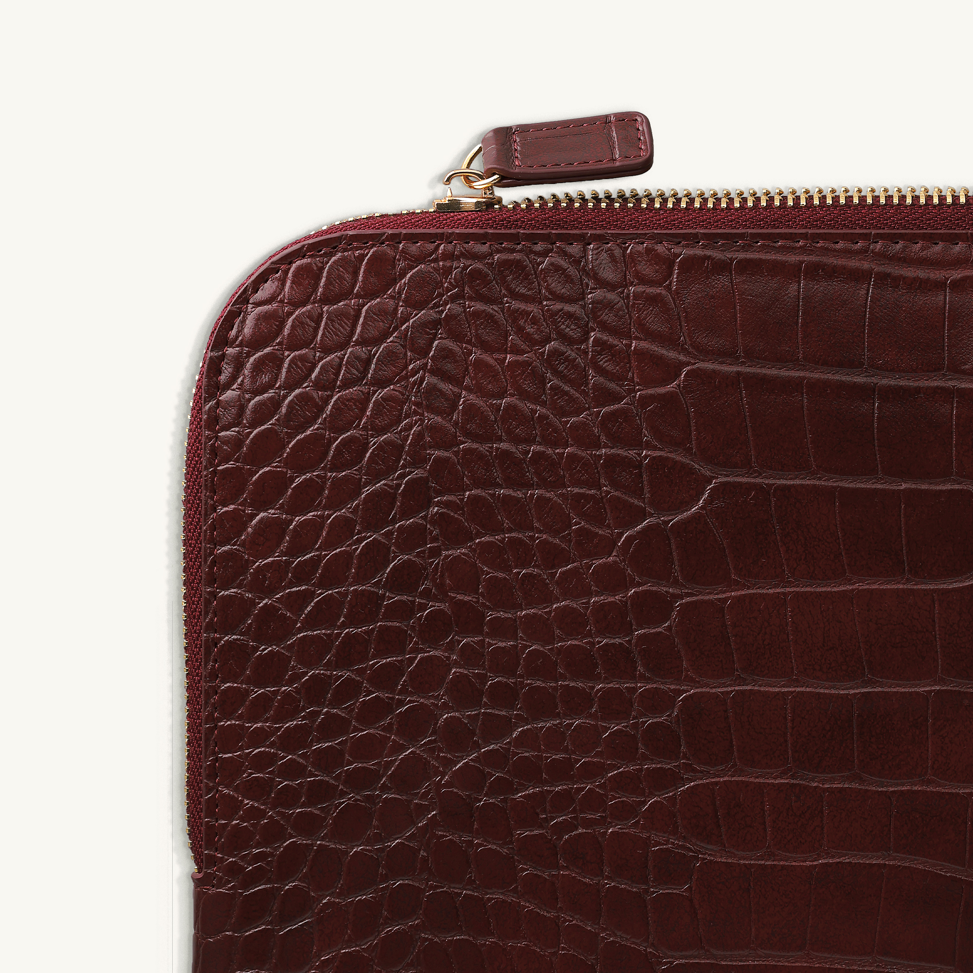 Dunkelrotes Kroko-Leder-Etui mit goldenem Reißverschluss und Anhänger.