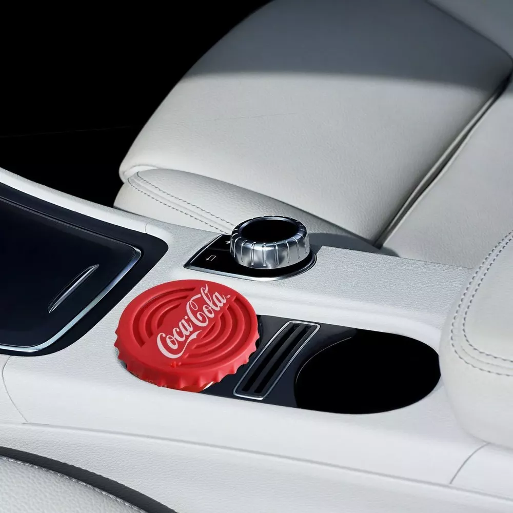Roter Coca-Cola-Flaschendeckel-Untersetzer auf einer weißen Autokonsole mit silbernem Knopf.