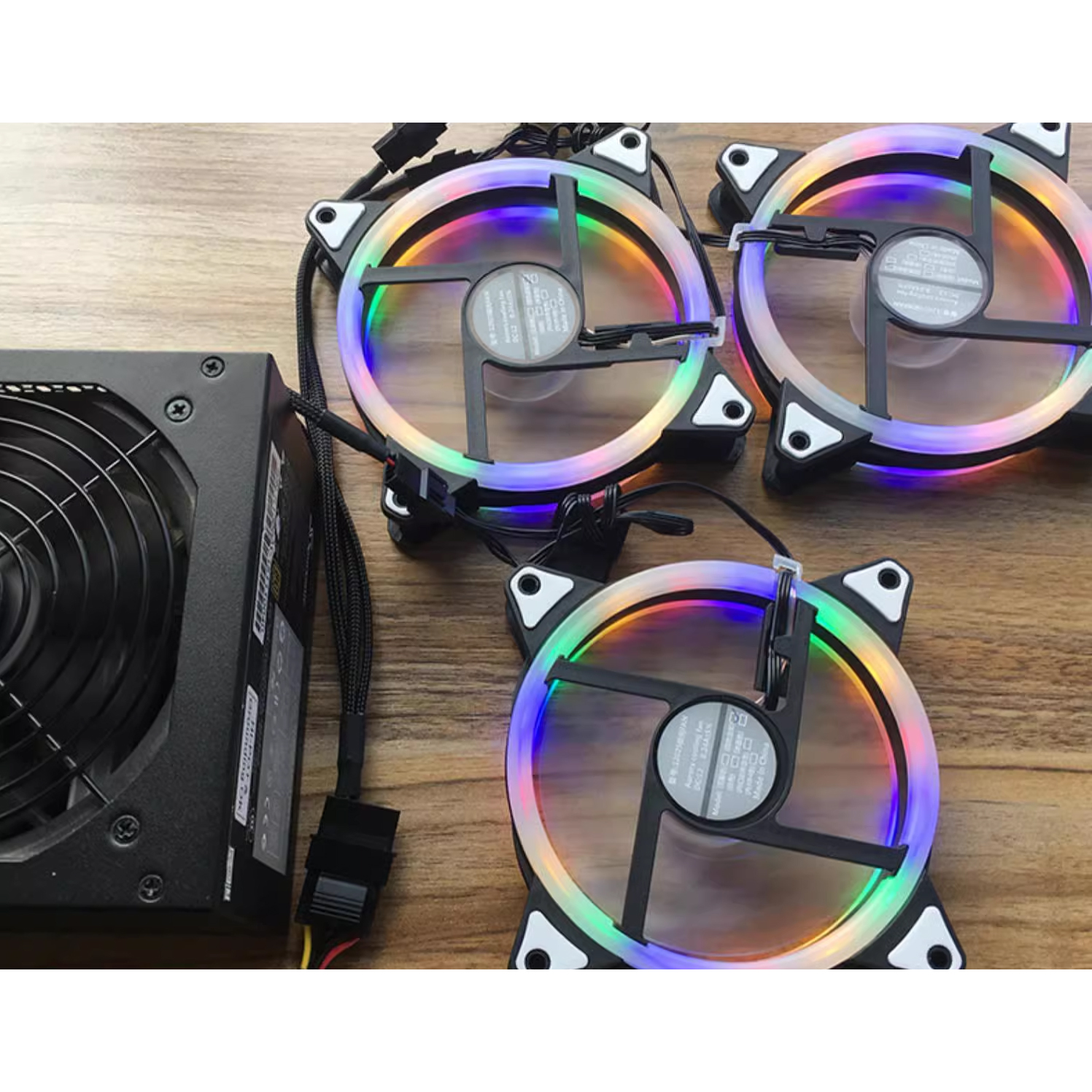 Ein Netzteil und drei bunte PC-Lüfter liegen auf einem Holztisch.