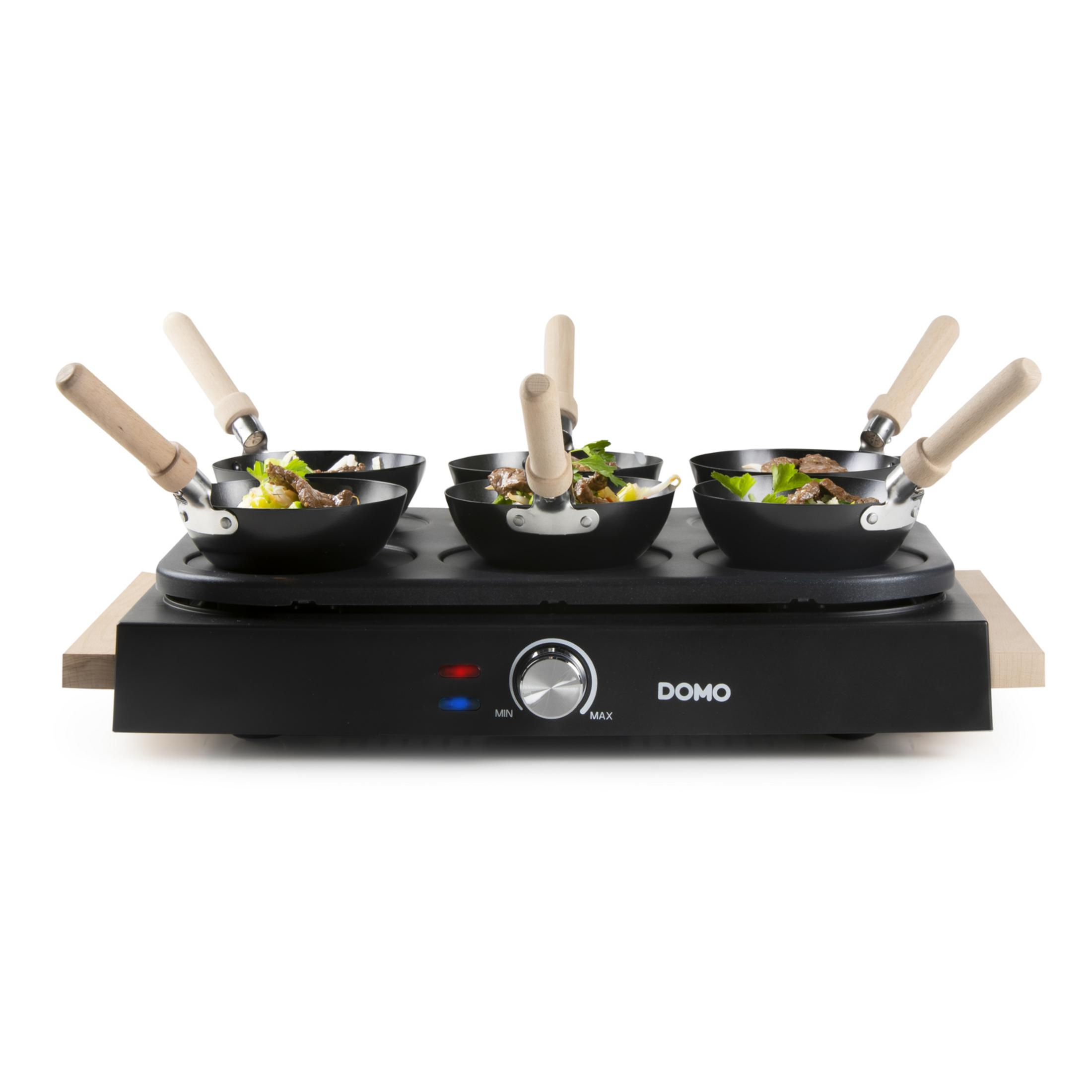 Ein schwarzes Raclette mit vier kleinen Pfannen und Holzgriffen, gefüllt mit Essen.