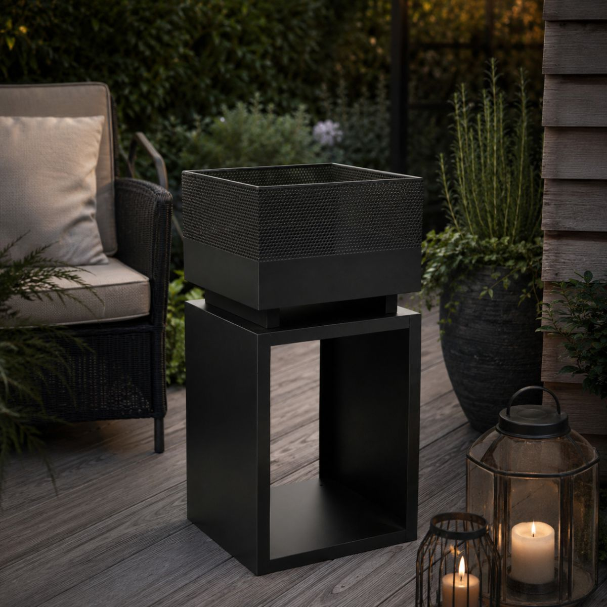 A black planter sits atop a cube table on a wooden deck. Candles glow nearby.