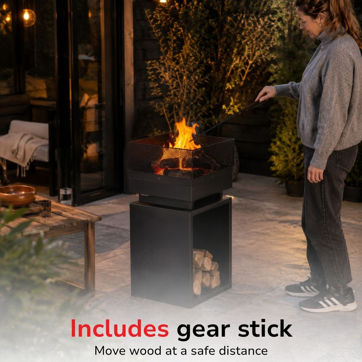Woman uses a gear stick to tend a fire pit with wood outdoors.