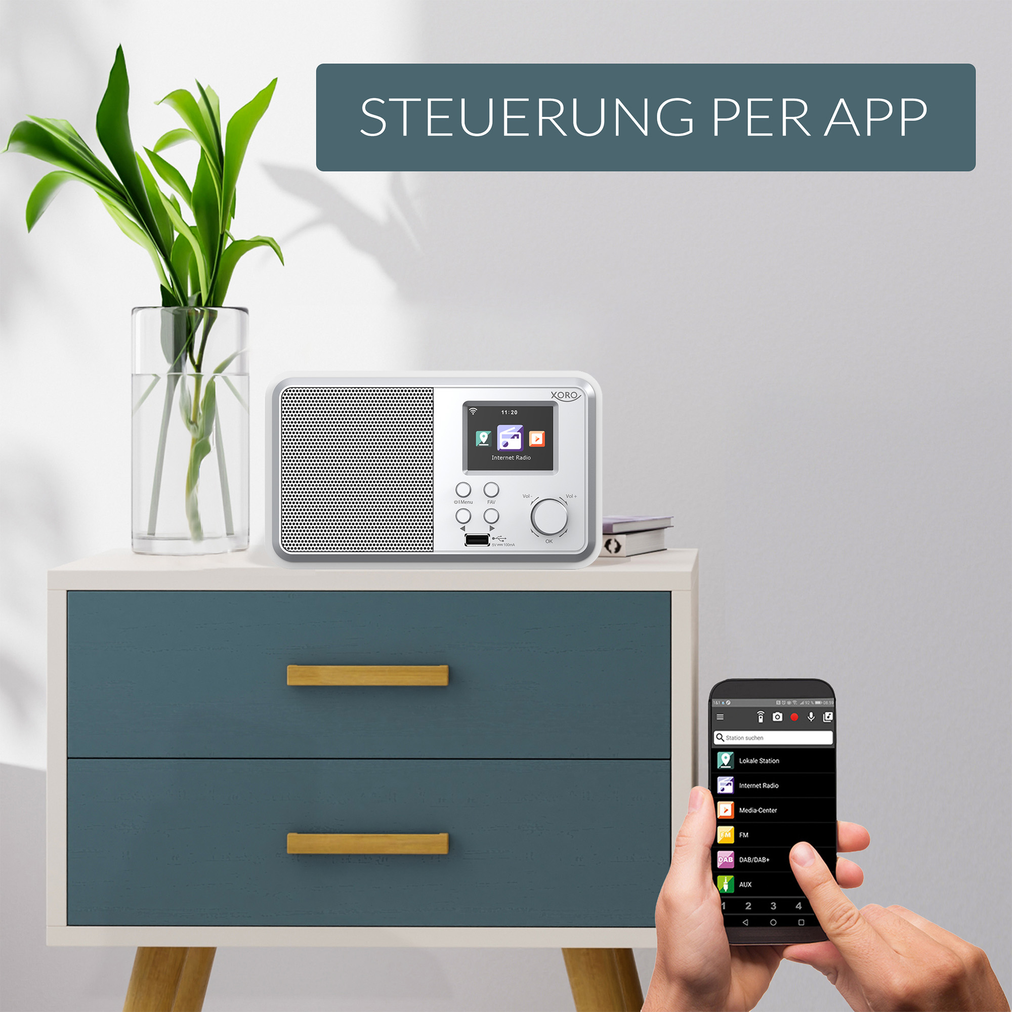 Ein weißes Radio mit Bildschirm steht auf einer Kommode. Eine App wird auf einem Handy gezeigt.