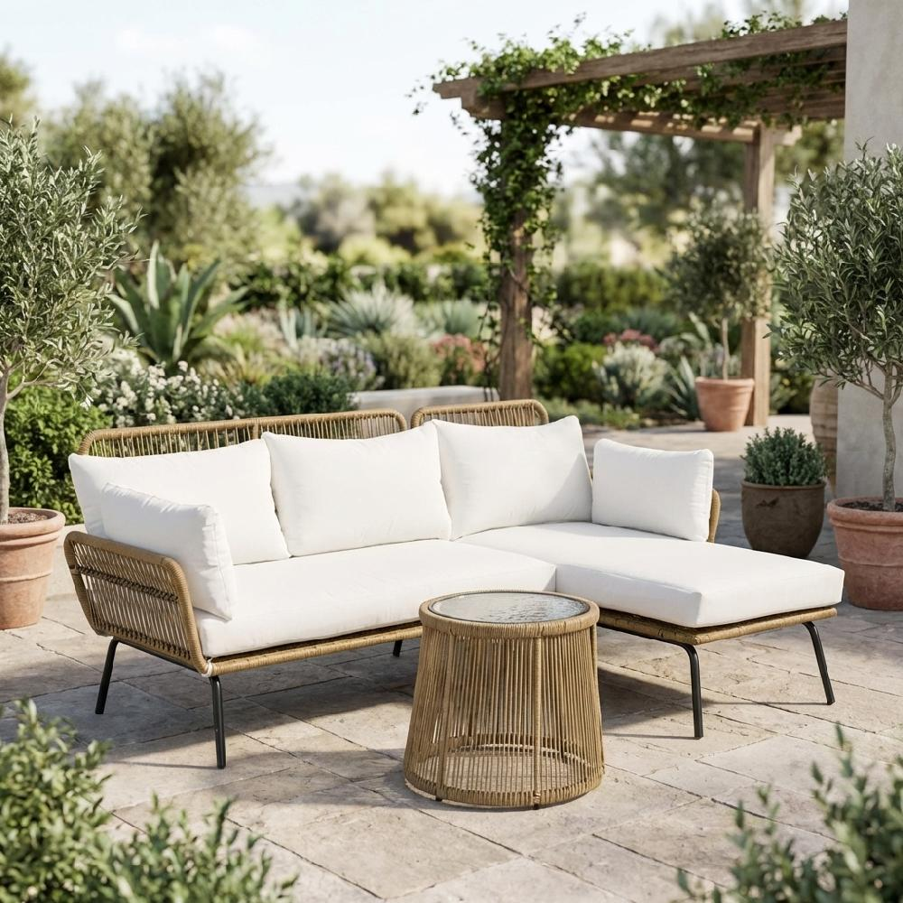 Divano componibile in vimini con cuscini bianchi e tavolino rotondo su patio in pietra.