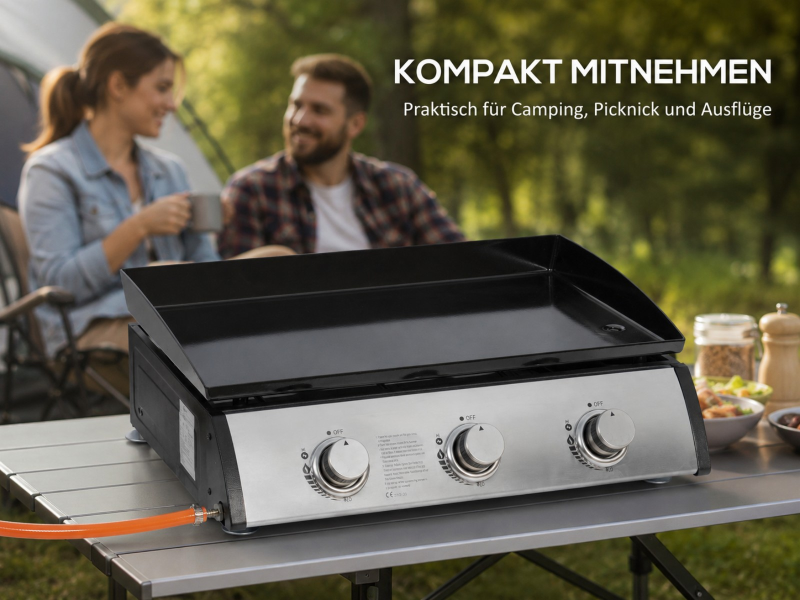 Ein Gasgrill steht auf einem Tisch, im Hintergrund ein Paar.