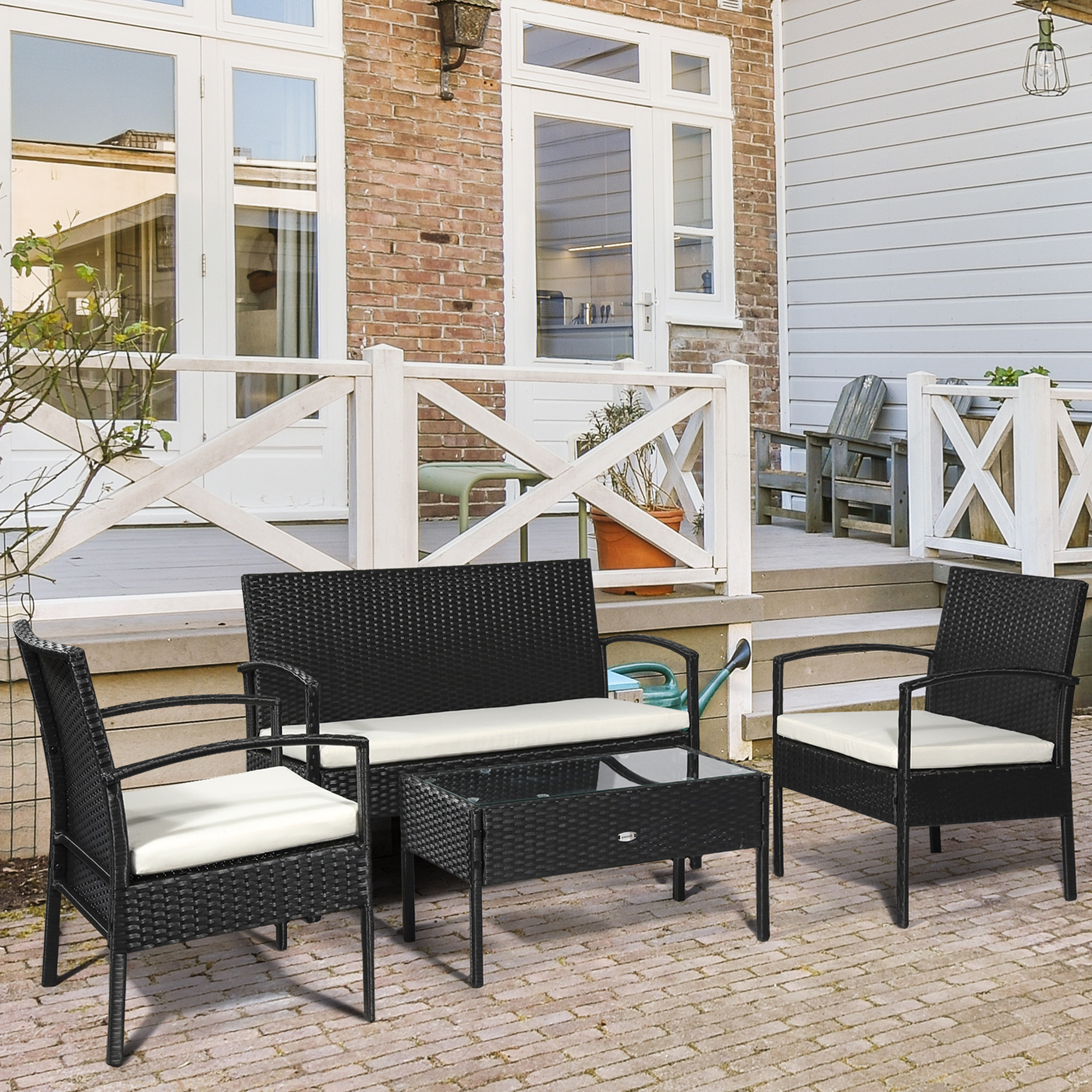 Divano in rattan nero con due poltrone e tavolino in vetro su un patio.