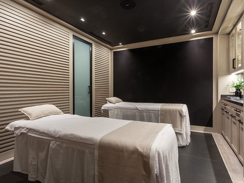 Dos camillas de masaje con sábanas blancas y mantas neutras en una sala de spa.