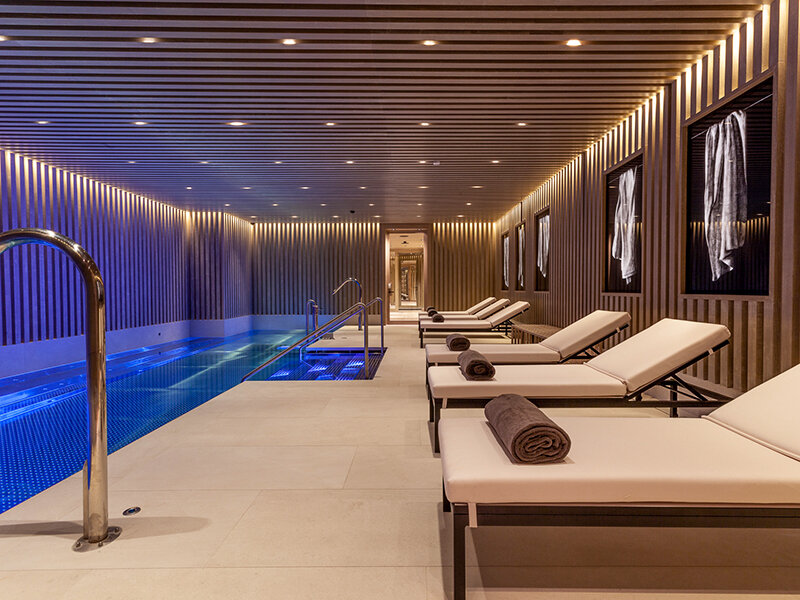 Una moderna zona de piscina interior con tumbonas, toallas e iluminación ambiental.