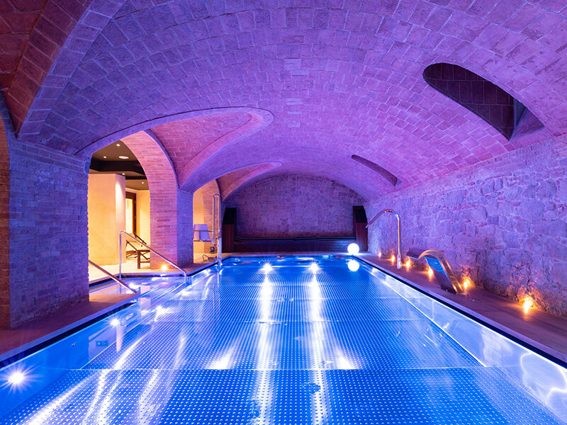 Piscina interior con luces azules bajo un techo abovedado de ladrillo.