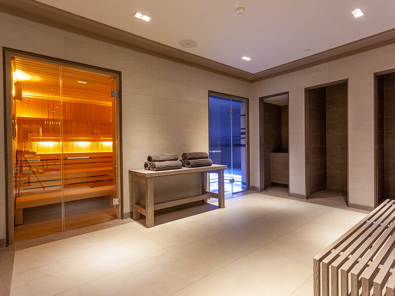 Un área de sauna con bancos de madera, puertas de vidrio, toallas y cabinas de ducha.