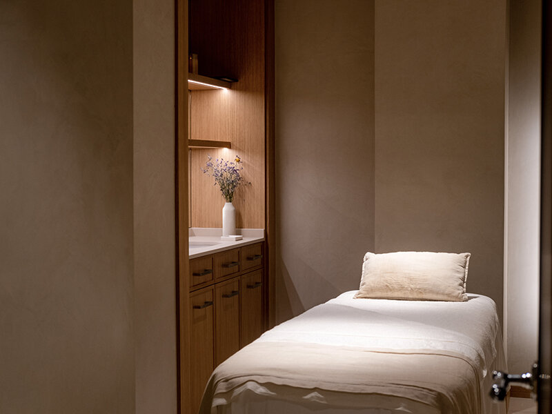 Una camilla de masaje con almohada en una habitación con armarios de madera y flores.