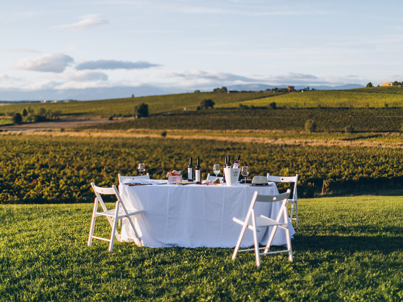 Una mesa puesta con vino y copas en un viñedo al atardecer.