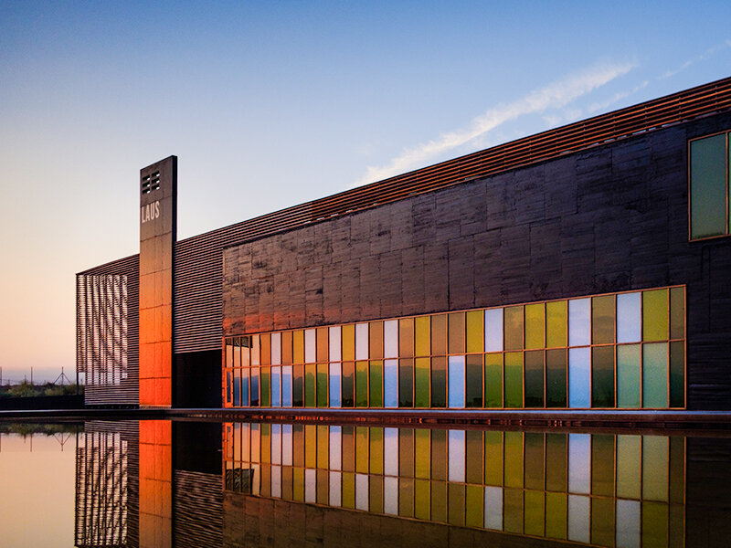 Edificio moderno con ventanas coloridas y reflejo en el agua al atardecer.