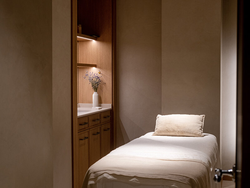 Una camilla de tratamiento con almohada en una habitación con armarios de madera y flores.